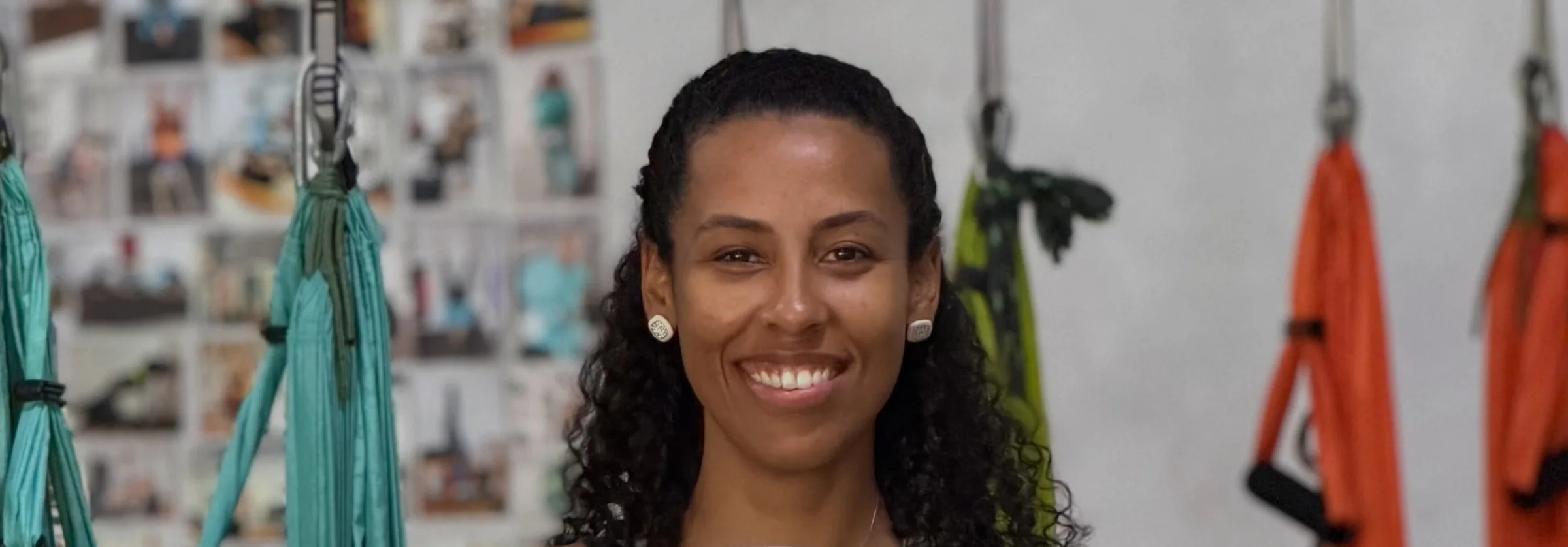 Aline Souza sorrindo no Studio, entre as redes verde-água e laranja do pilates aéreo